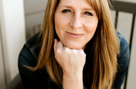 Photo of speaker Holly Schneider wearing a black jean jacket and sitting in a rocking chair on a porch.