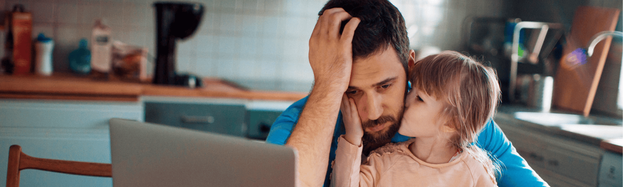 Dad looking distressed in front of his computer and bills with his daughter on his lap.